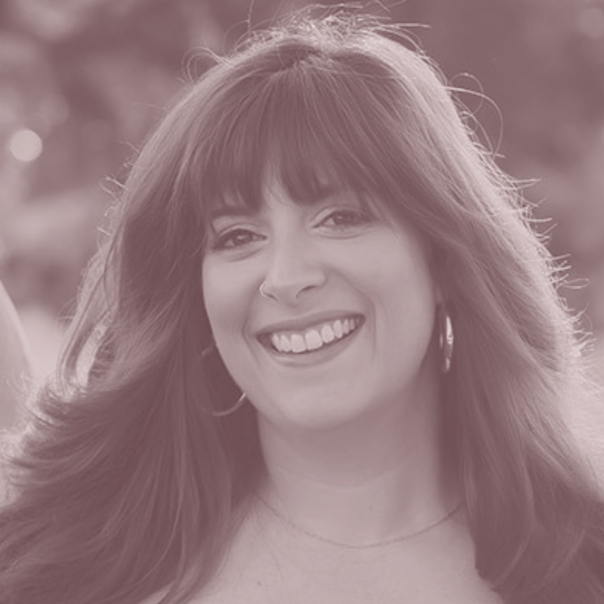 Close-up portrait of a smiling woman with long hair and bangs wearing hoop earrings and a subtle necklace.