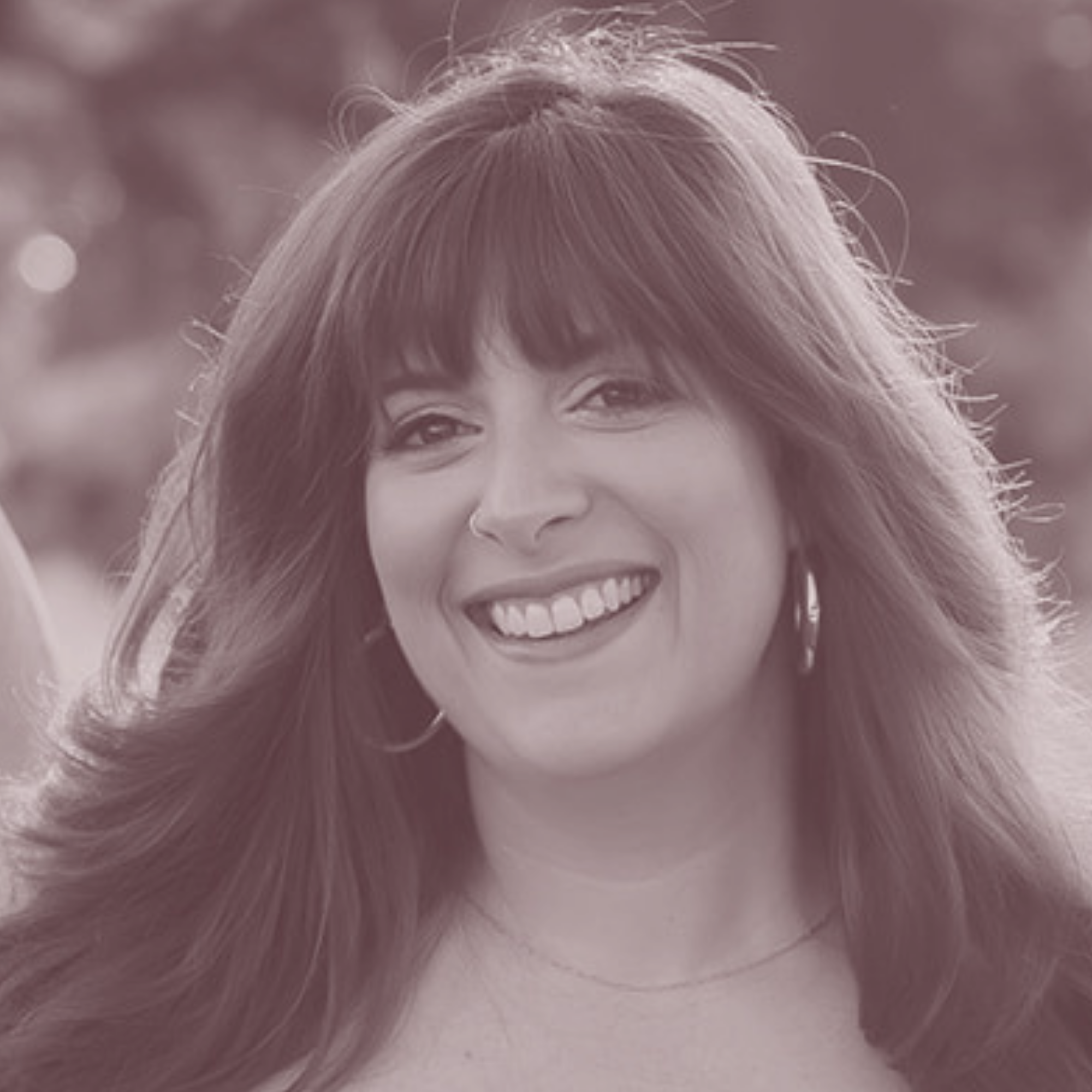 Close-up portrait of a smiling woman with long hair and bangs wearing hoop earrings and a subtle necklace.