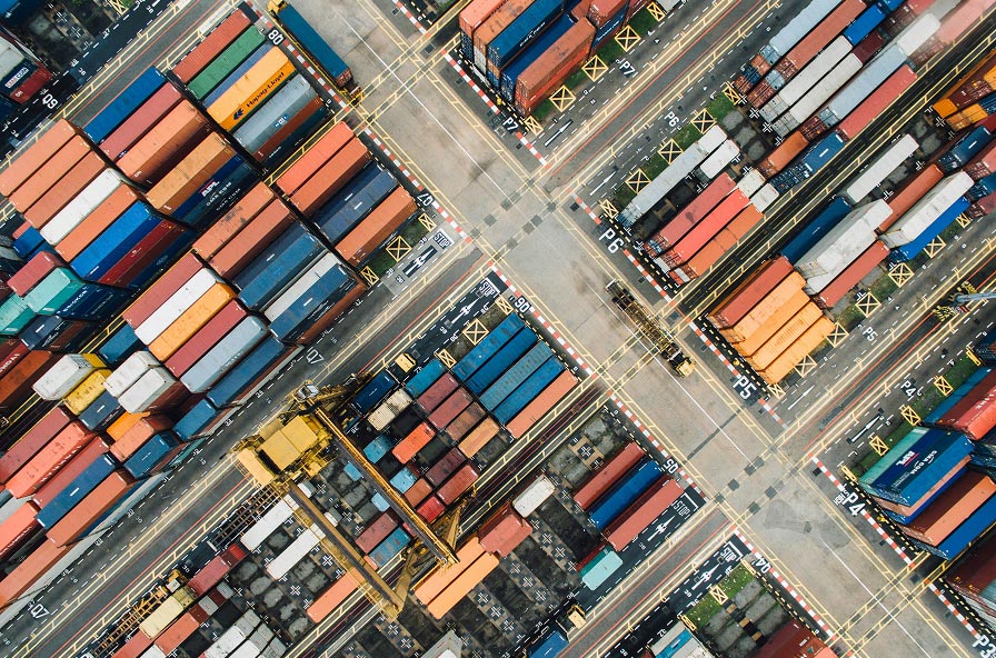 Aerial view of a container yard with several red automated guided vehicles transporting cargo containers numbered 825, 811, 855, and 711.