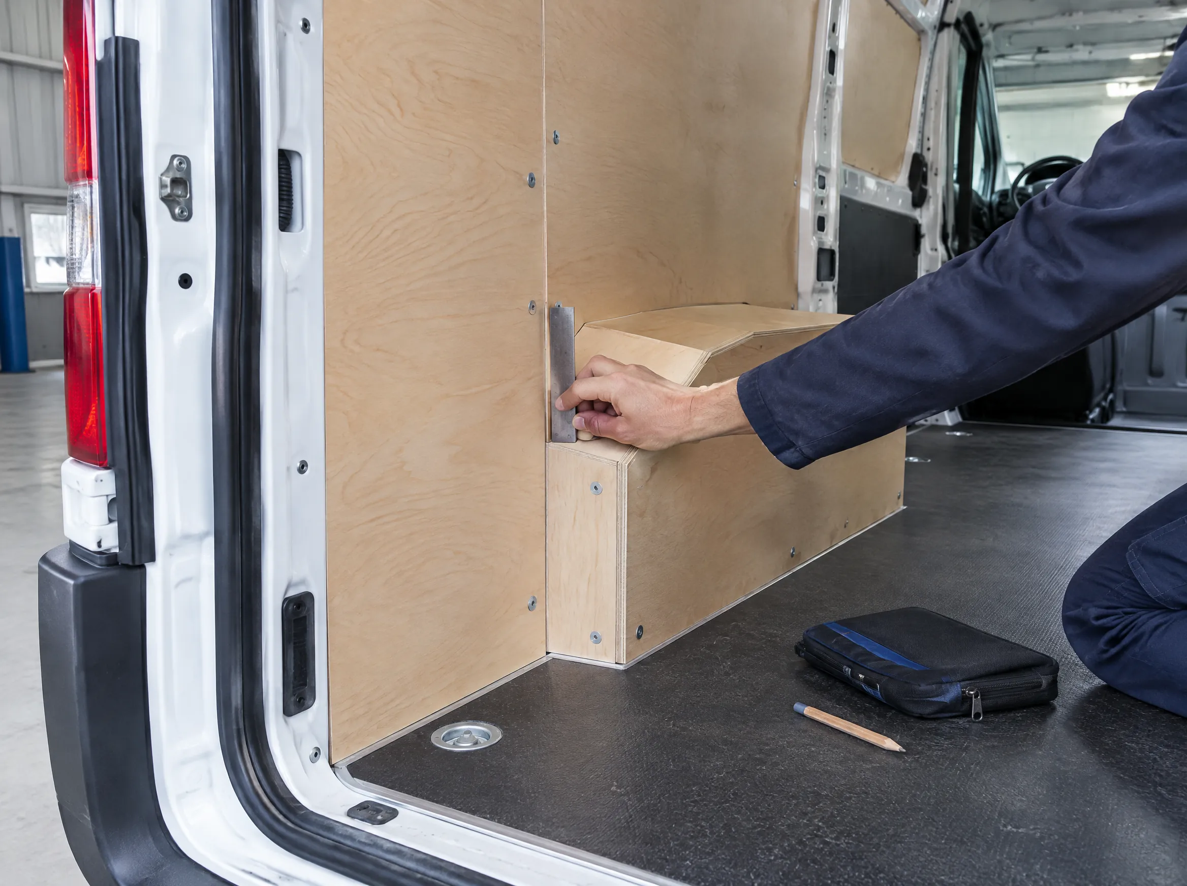 Illustrative detail of fitted plywood panels and a wheel-arch box inside a van.