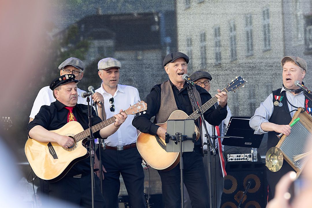 Musikere synger og spiller på en utendørsscene under 17. mai-feiringen i Bergen.