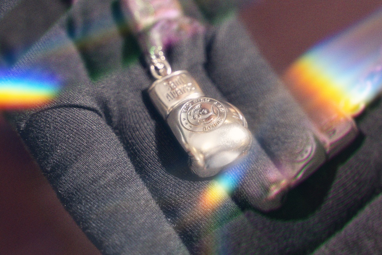 Silver boxing-glove pendant held in a black glove