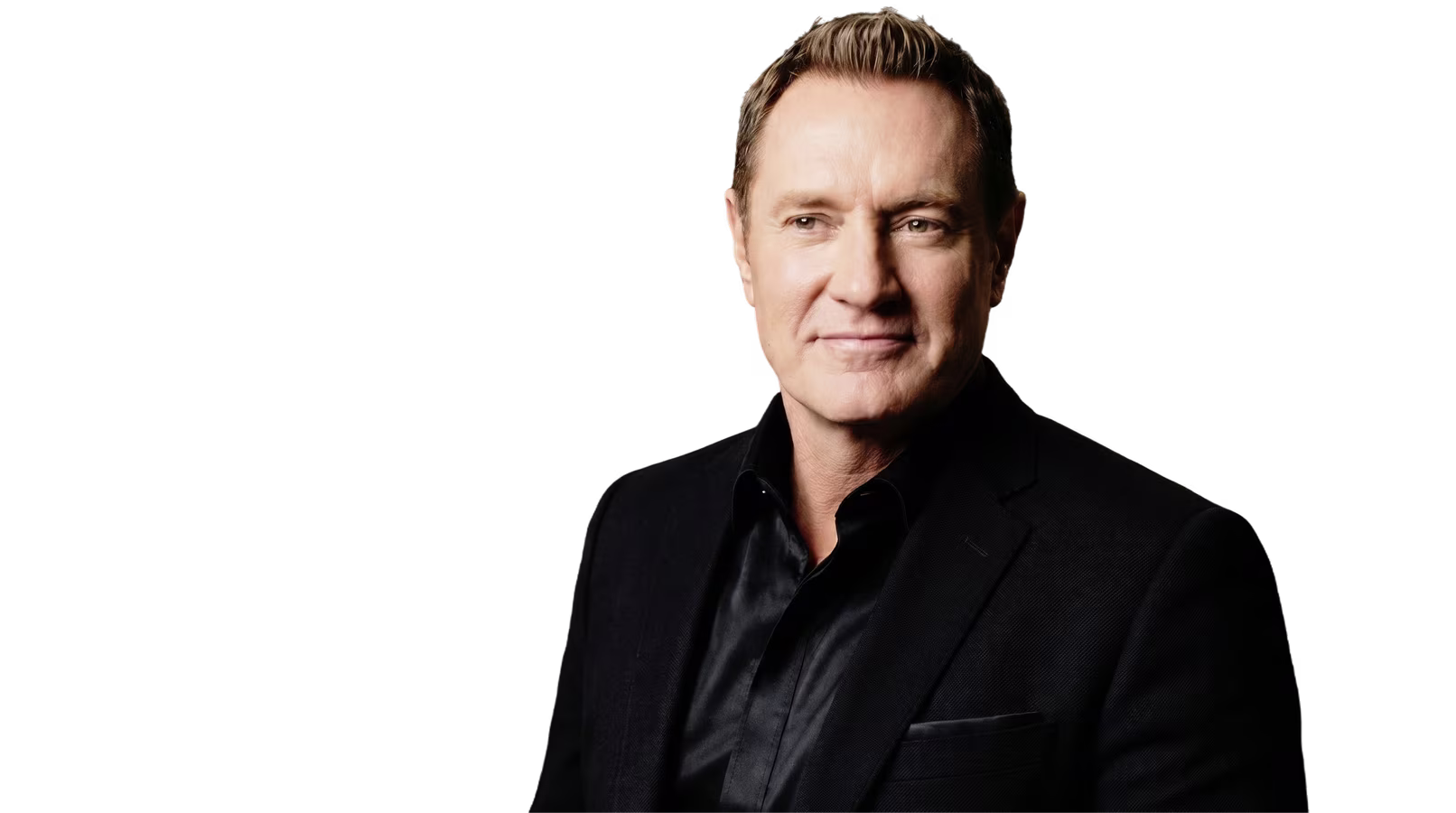 Darren Hardy in a dark jacket and black open-collar shirt, smiling at the camera