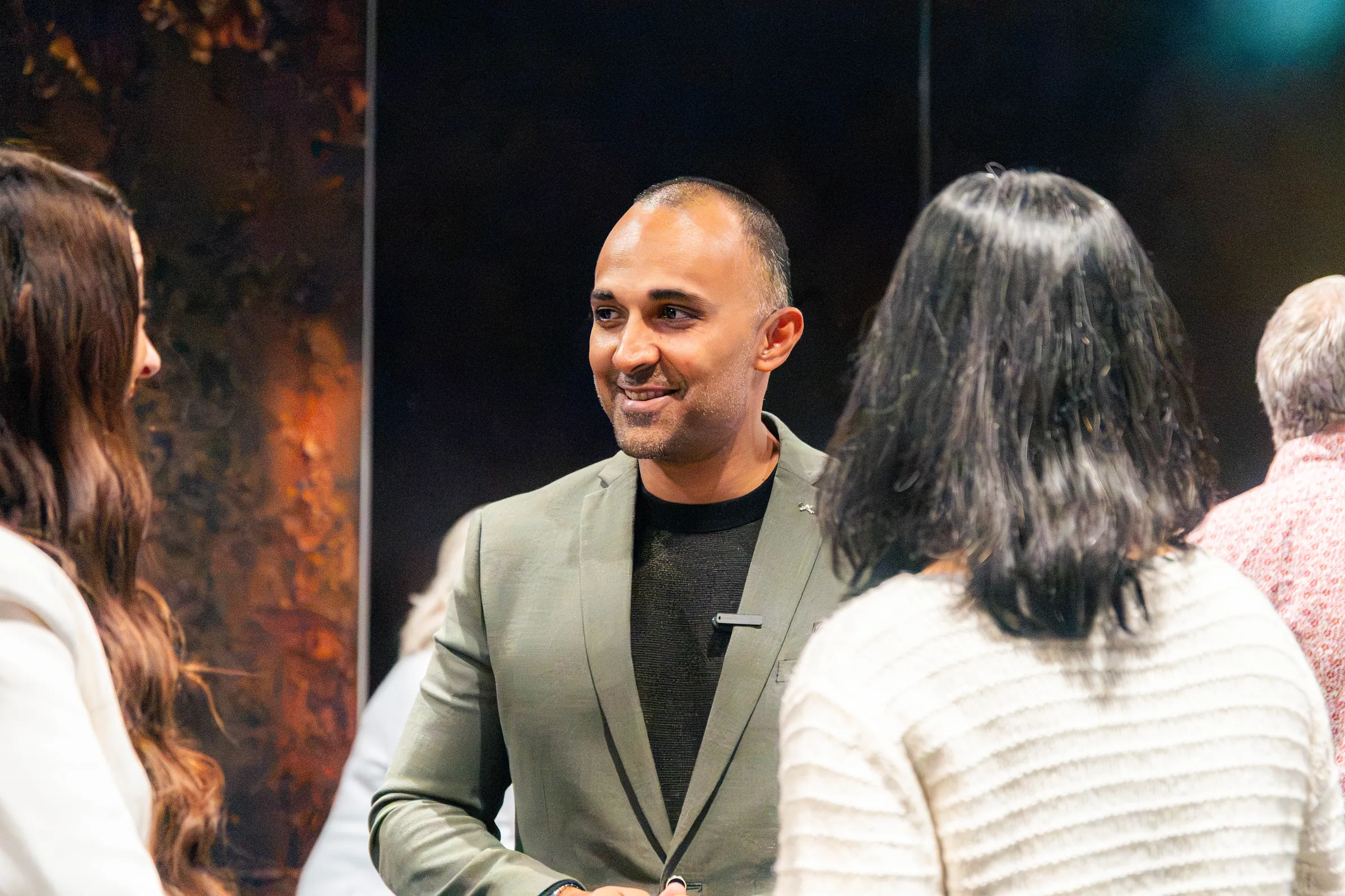 A man in a green jacket talking with two women at a Perth event, photographed by Growth Concept Media.
