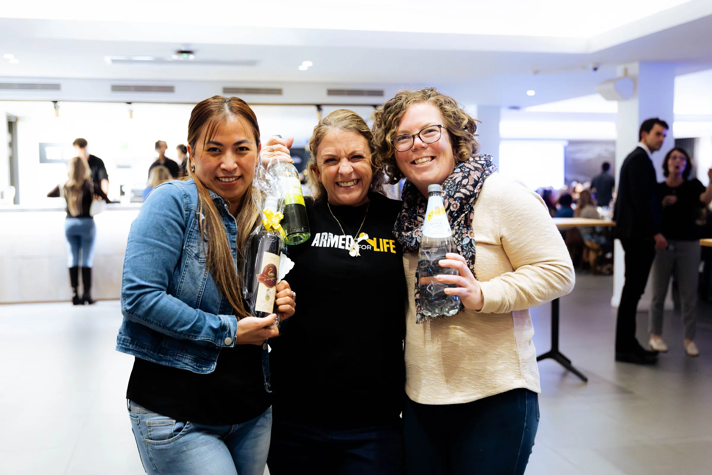 Three guests posing with bottles at the Armed For Life quiz night at The Hall, The Camfield, Burswood.