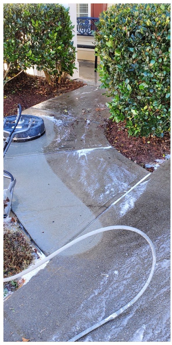 Concrete walkway mid-cleaning with a surface cleaner showing the dirty and clean halves