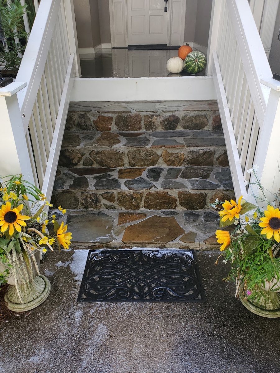 Stone front steps and porch clean after pressure washing, with fall flowers on either side