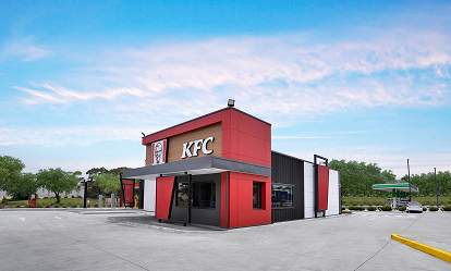 Modern KFC restaurant building with red and black exterior under a partly cloudy blue sky, surrounded by a parking lot and greenery.