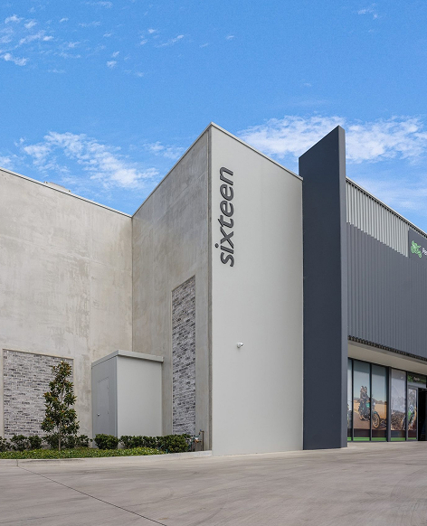 Modern commercial building with a tall vertical sign displaying the word 'sixteen' against a clear blue sky.
