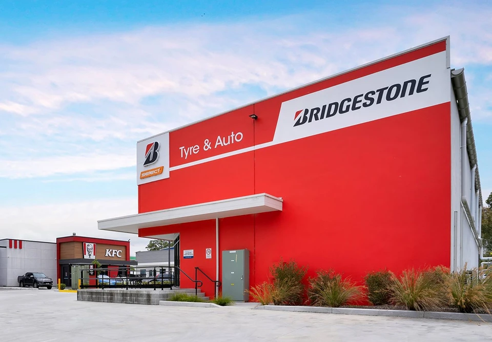 Red Bridgestone Tyre & Auto building with a white and red awning, adjacent to a KFC restaurant under a partly cloudy sky.