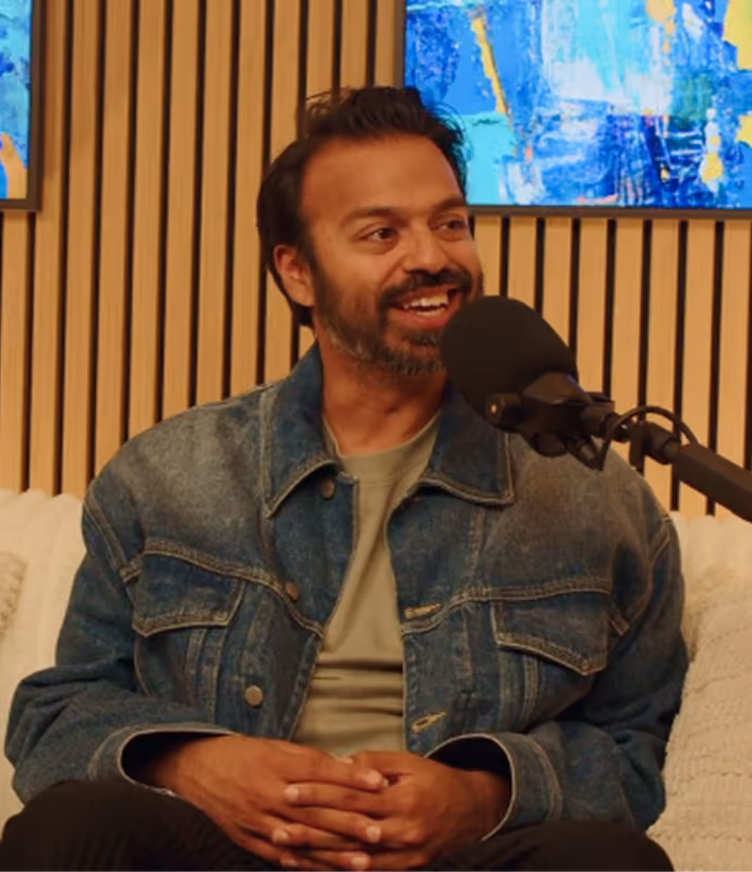 Un homme souriant en veste en jean parle dans un micro lors de l'enregistrement d'un podcast.
