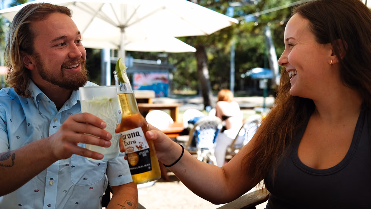 Two friends clink a beer and a drink together under the umbrellas in the beer garden.