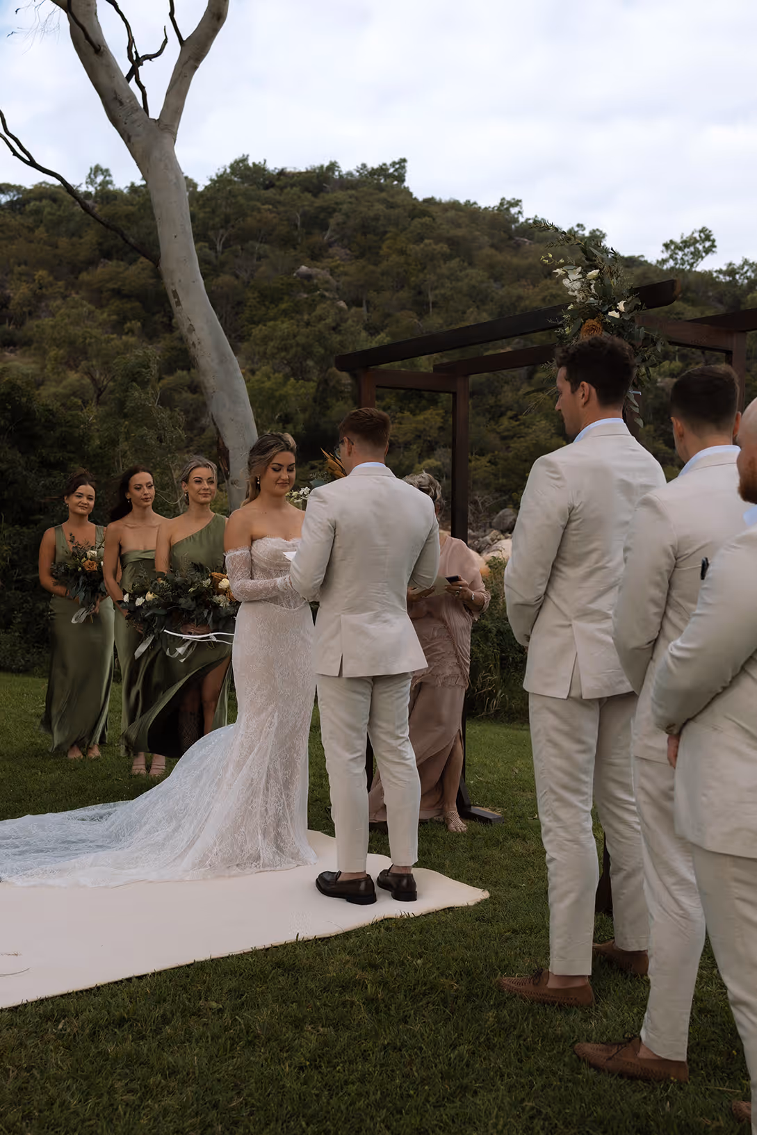 A wedding party gathered on the lawn, bridesmaids in green and groomsmen in cream.