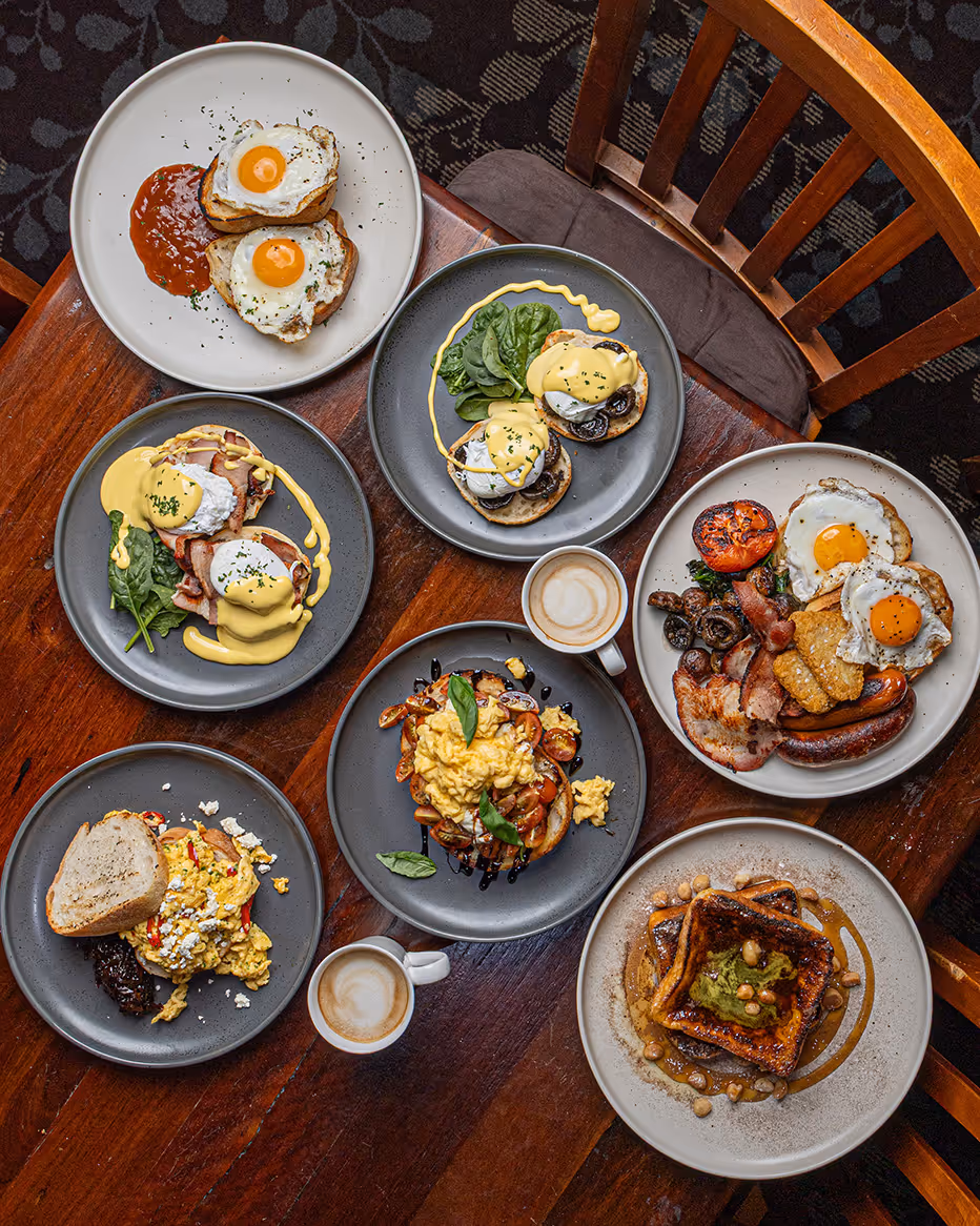 A breakfast spread of eggs benedict, waffles and coffee shared across the table.