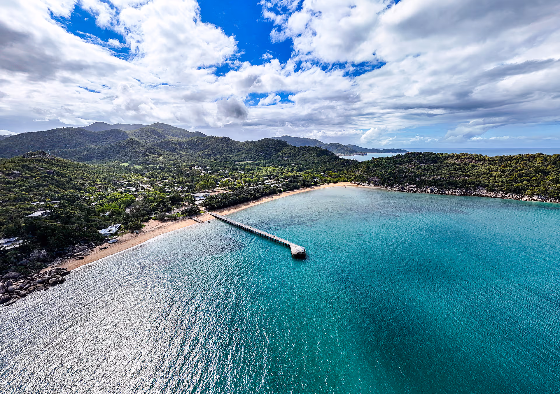 An aerial view of Picnic Bay, its jetty reaching out over clear turquoise water.