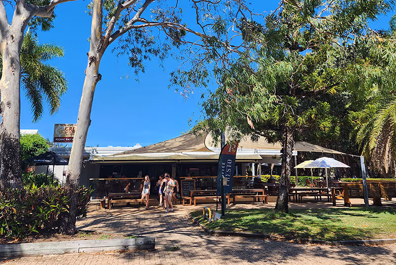 Picnic Bay Hotel seen from the street, its open-air terrace shaded by tall gum trees.