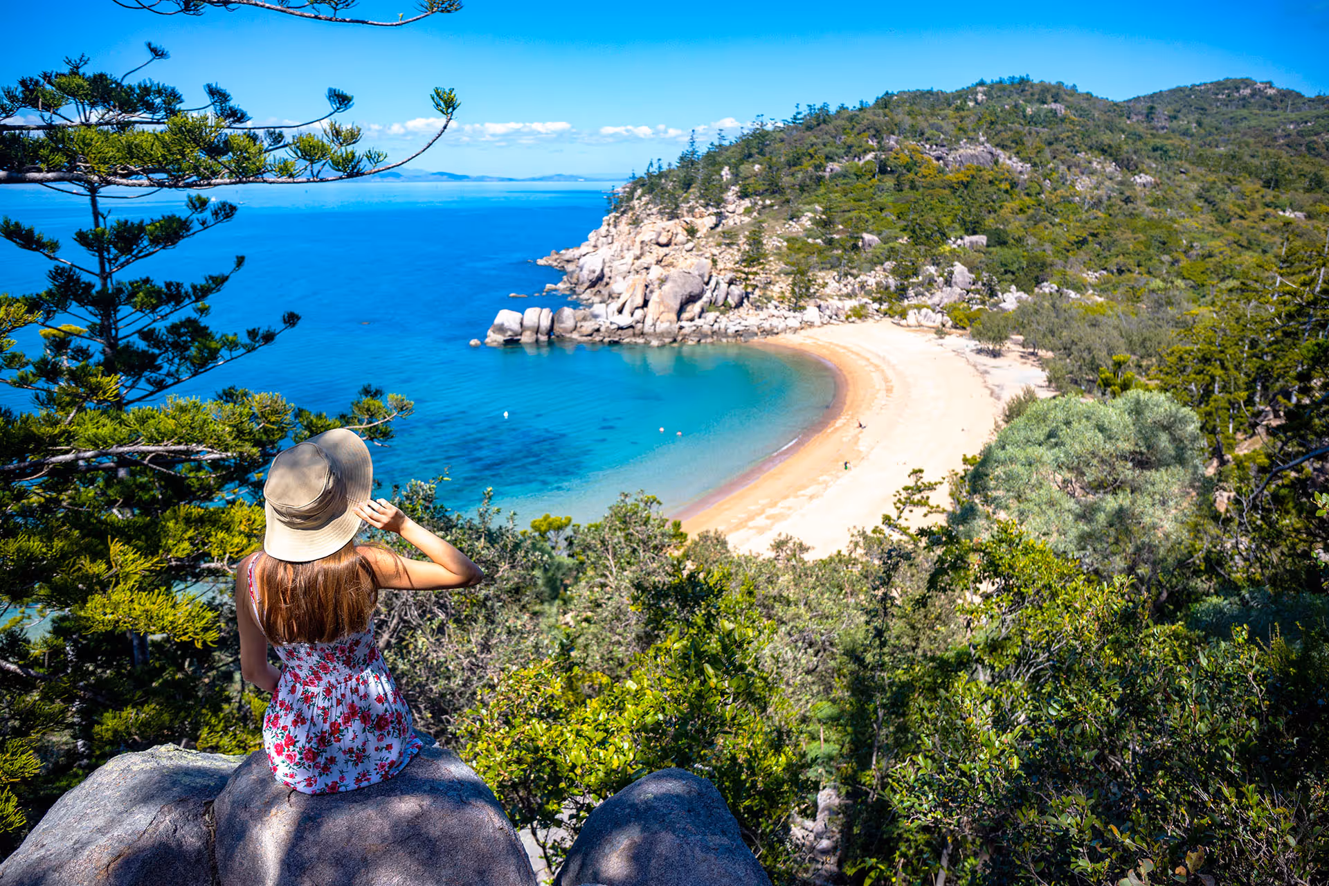 A visitor in a sun hat takes in the view over a turquoise bay from a Magnetic Island lookout.