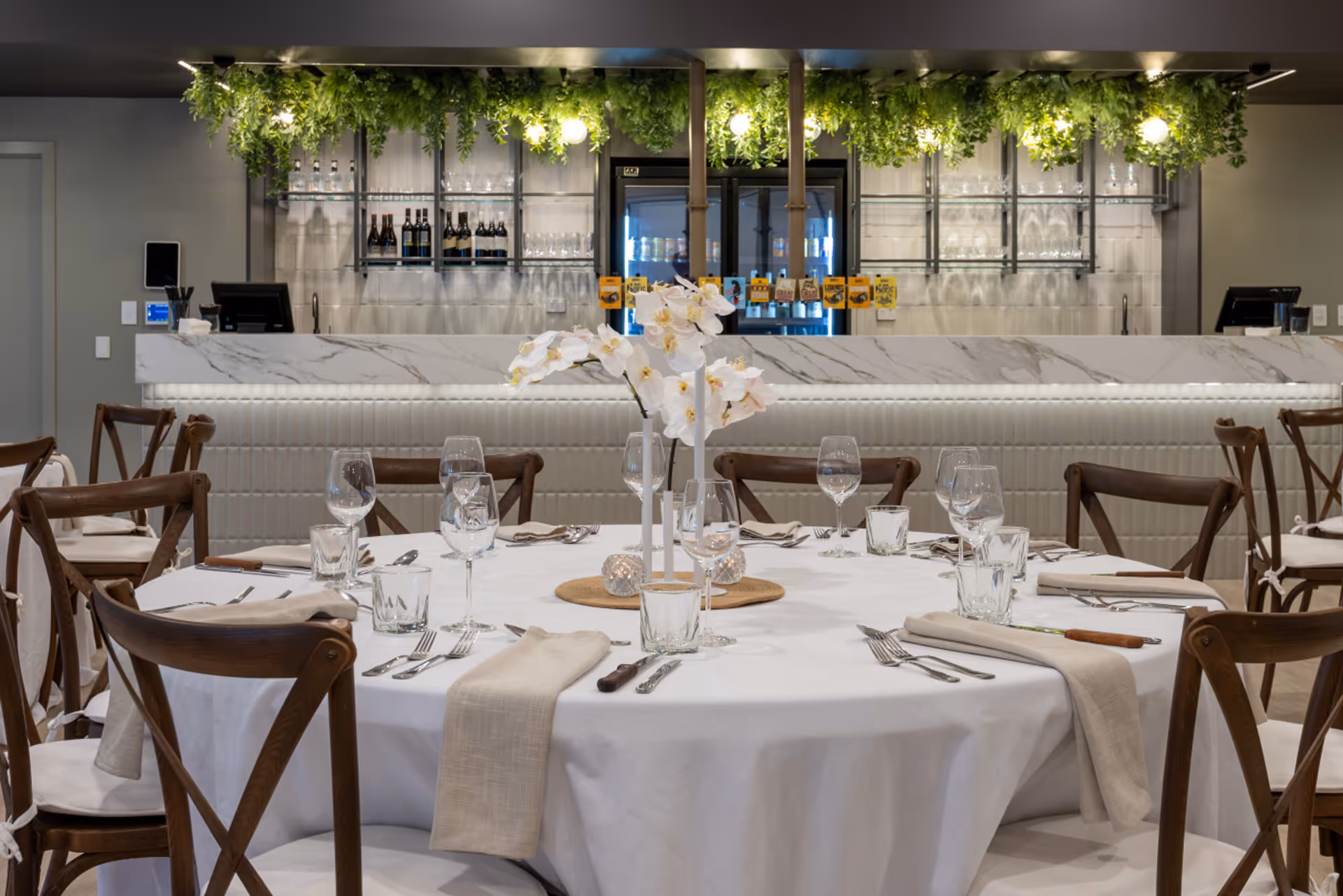 A long banquet table dressed with white orchids, glassware and trailing greenery.