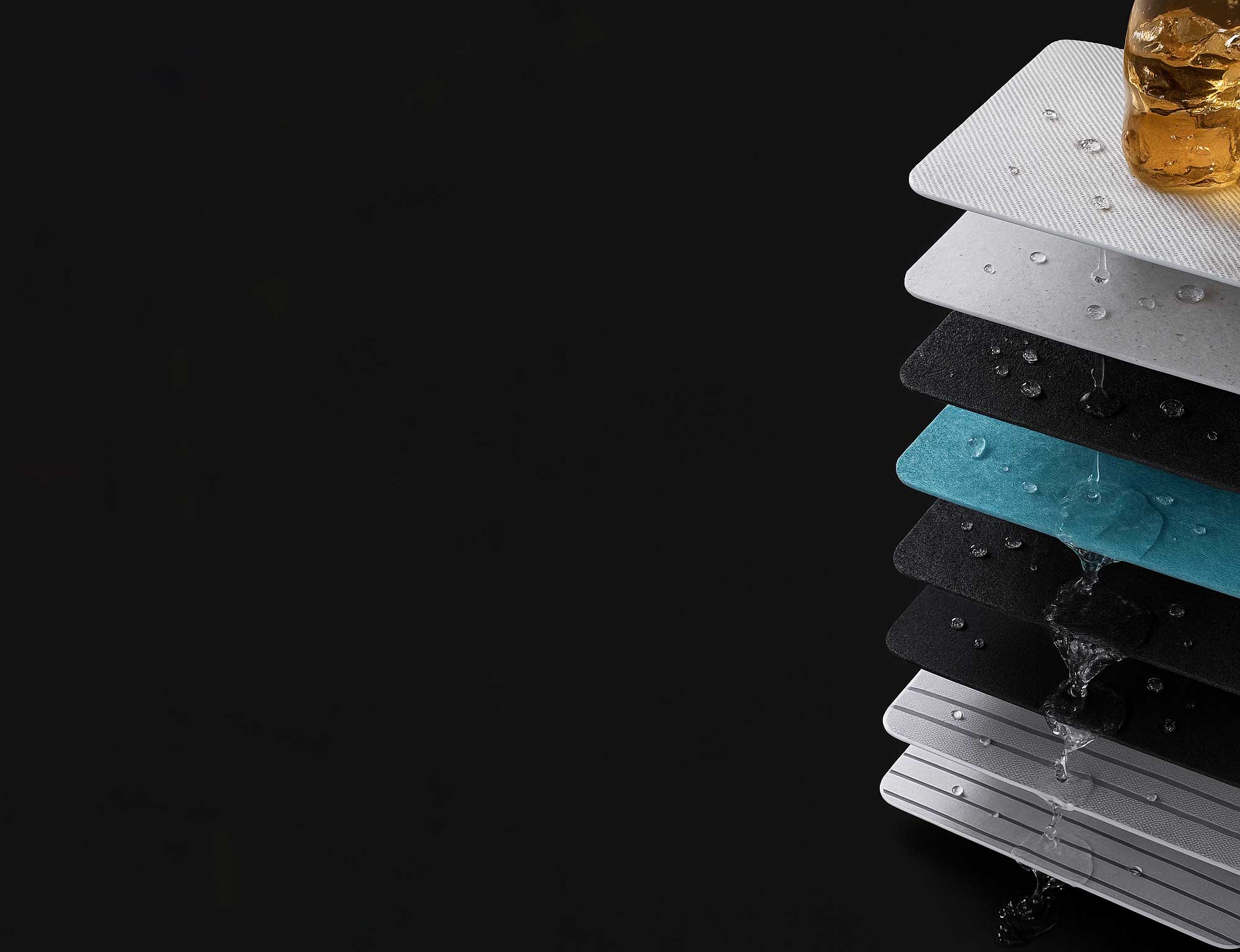 Stack of various textured and colored rectangular material samples with water droplets and small ice cubes on them, showing water resistance or waterproof features against a black background.
