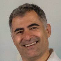 Smiling middle-aged man with short gray hair and light skin, wearing a white collared shirt against a plain light background.