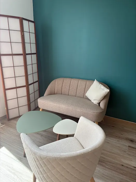 Le cabinet : un canapé et un fauteuil clairs, une table basse vert d'eau et un paravent, devant un mur bleu canard