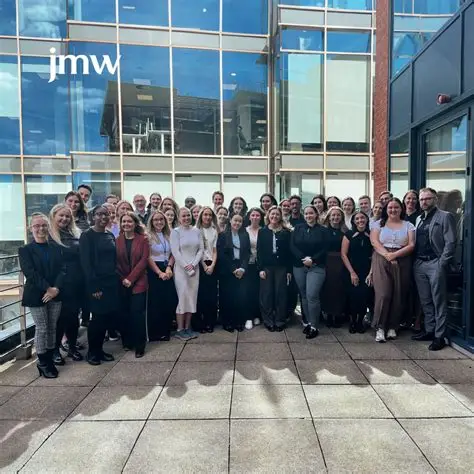 JMW Solicitors team gathered outside a glass-fronted office with JMW signage
