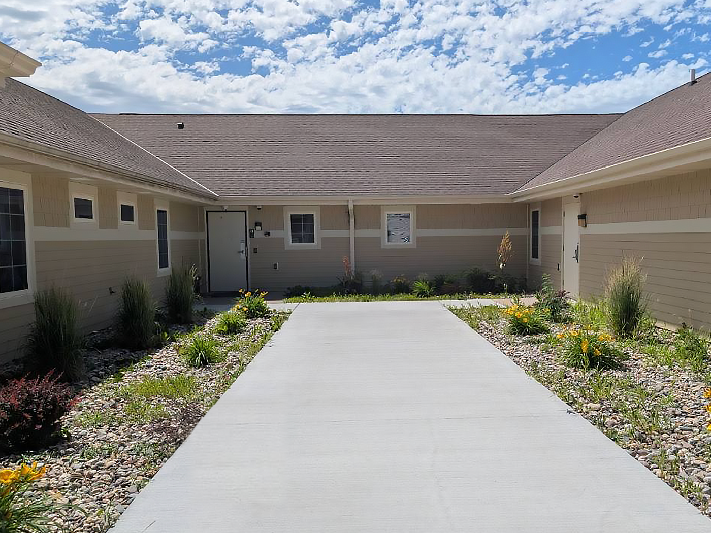 A paved walkway through a landscaped courtyard between the wings of a single-story building.