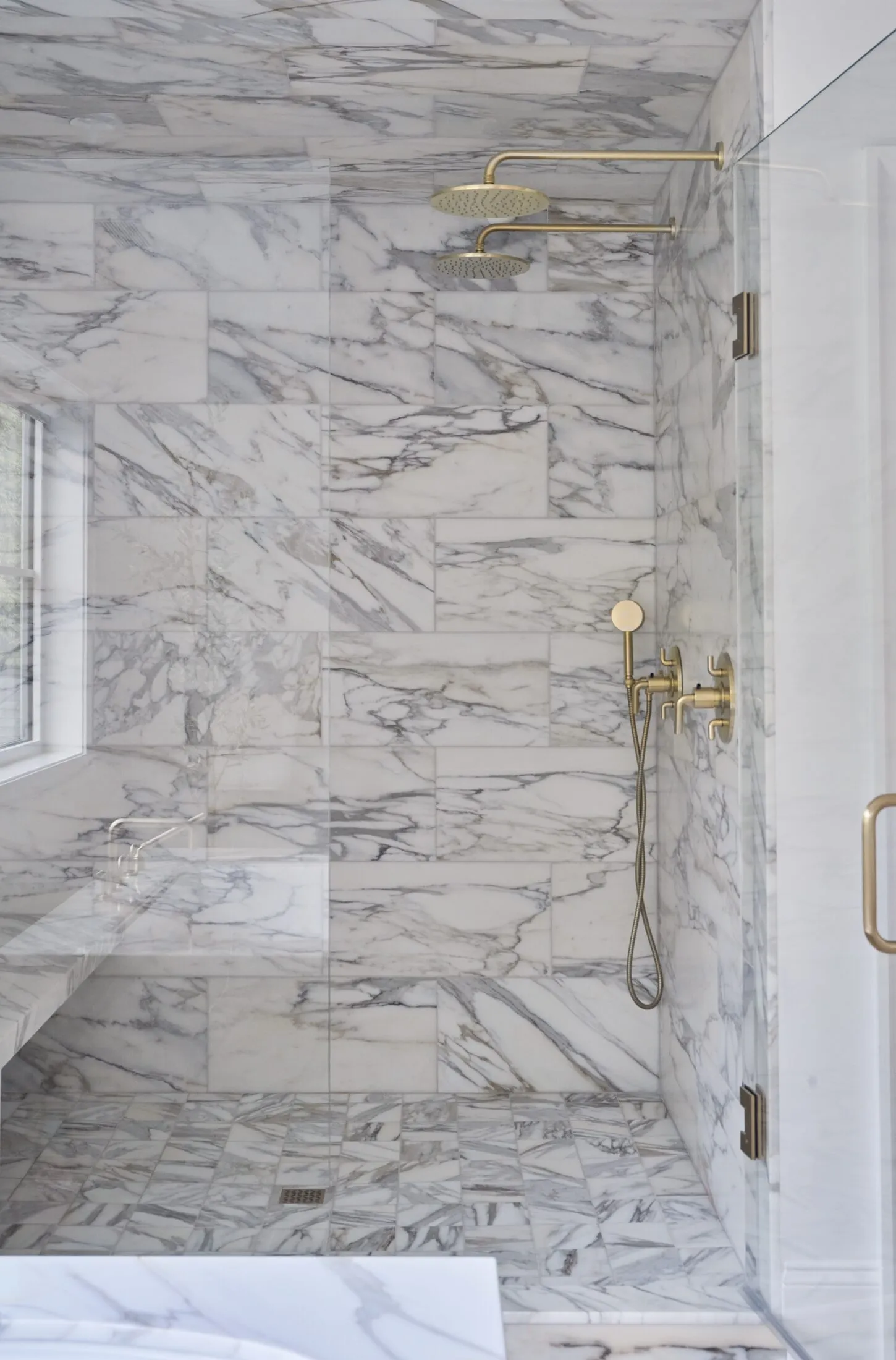 Calacatta marble shower with twin brass rain heads and a built-in bench