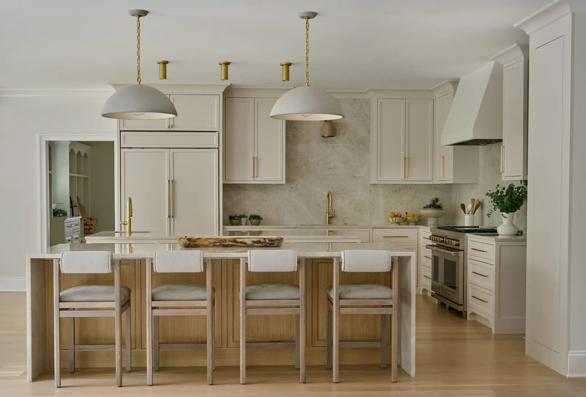 Cream kitchen with a marble island, plaster hood and white oak counter stools.