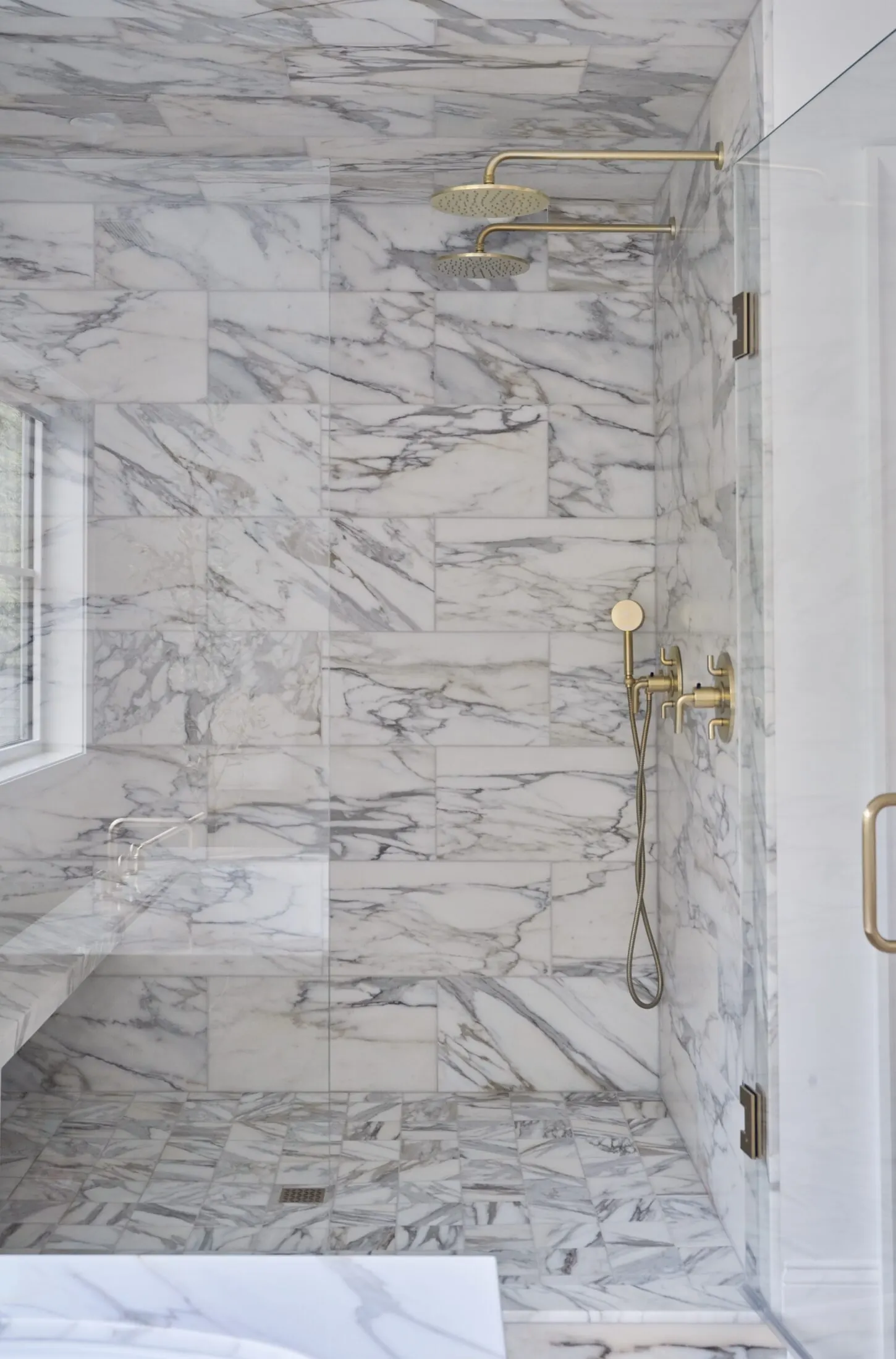Calacatta marble shower with a brass rain head and a built-in bench