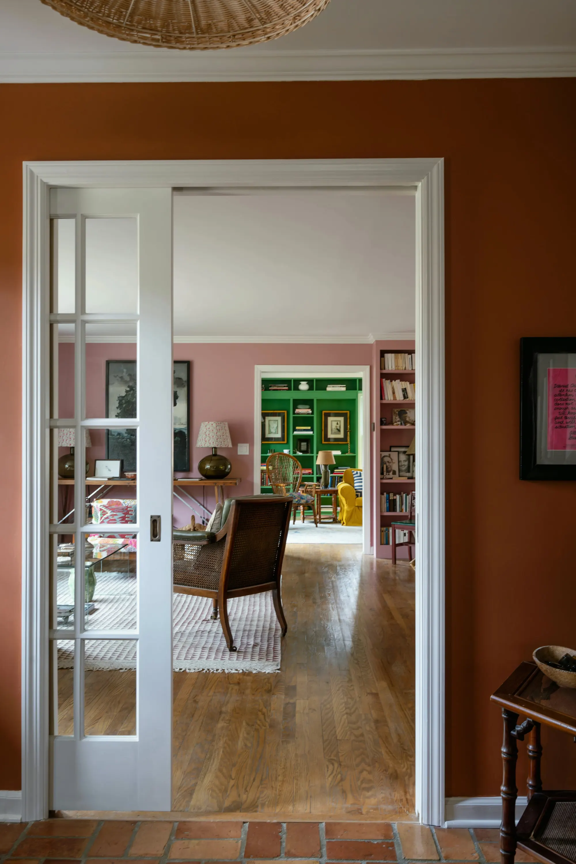 Terracotta hall with white pocket doors opening through a rose room to an emerald green library