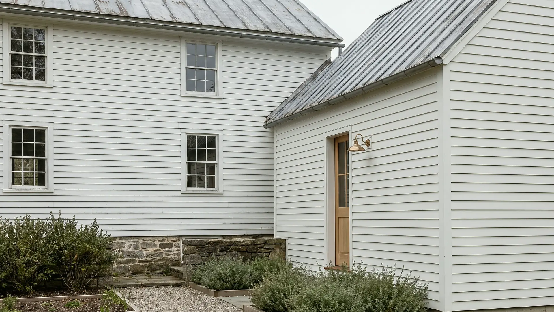 A white clapboard farmhouse with a standing-seam metal roof and a lower wing