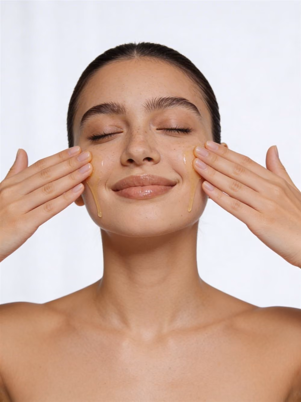 Smiling woman applying serum to her cheeks with both hands