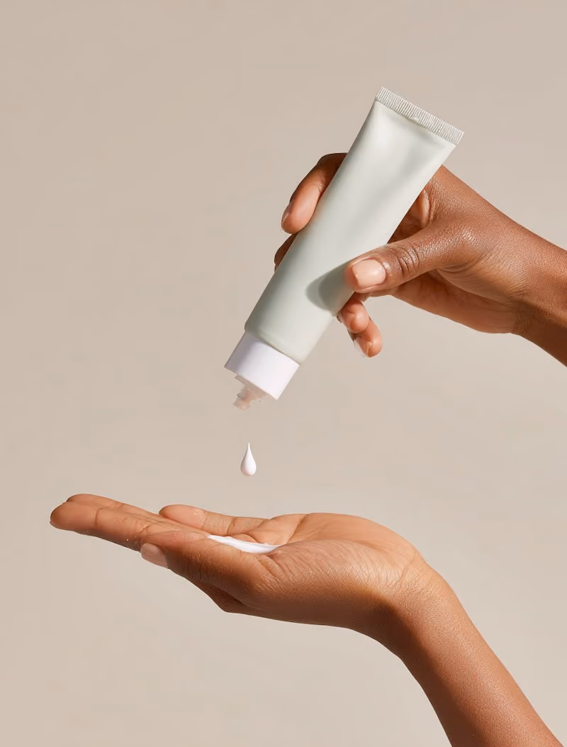 Hands dispensing a drop of cream from a pale green tube