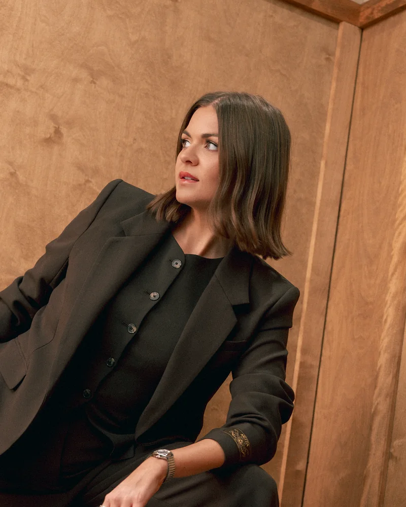 Kaylin Harding in a black suit against burl wood.