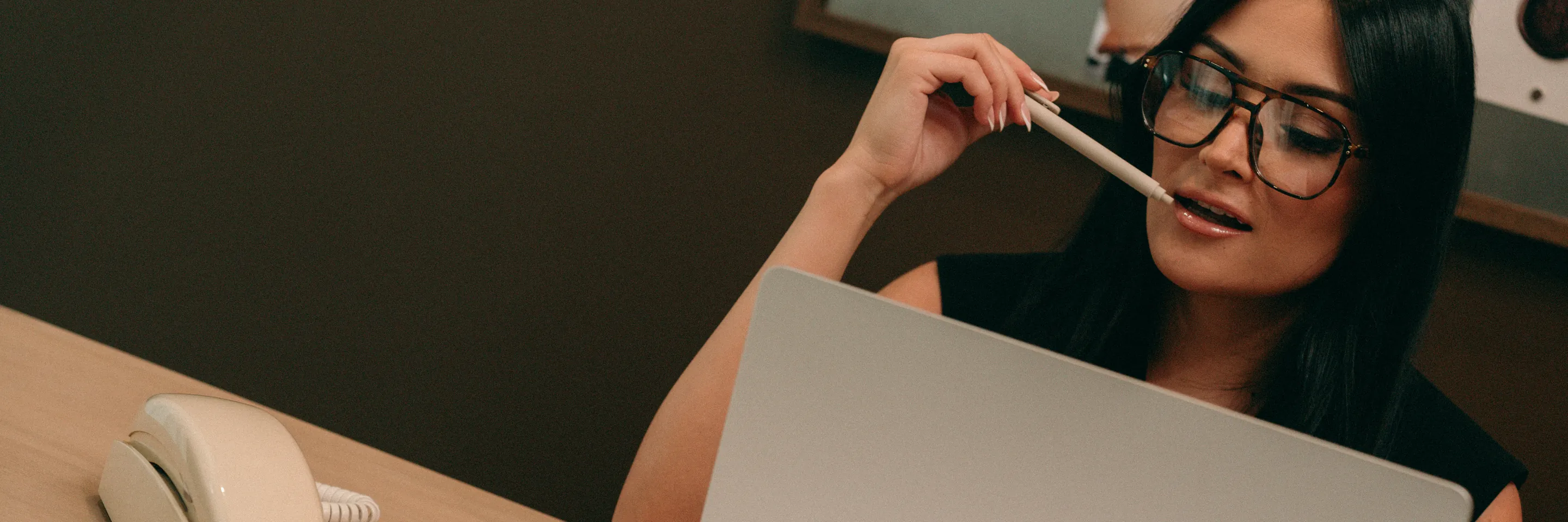 A strategist at her laptop, pencil in hand, reviewing reports at her desk.