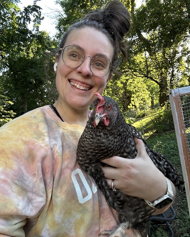 Molli in her backyard, smiling and holding a speckled hen