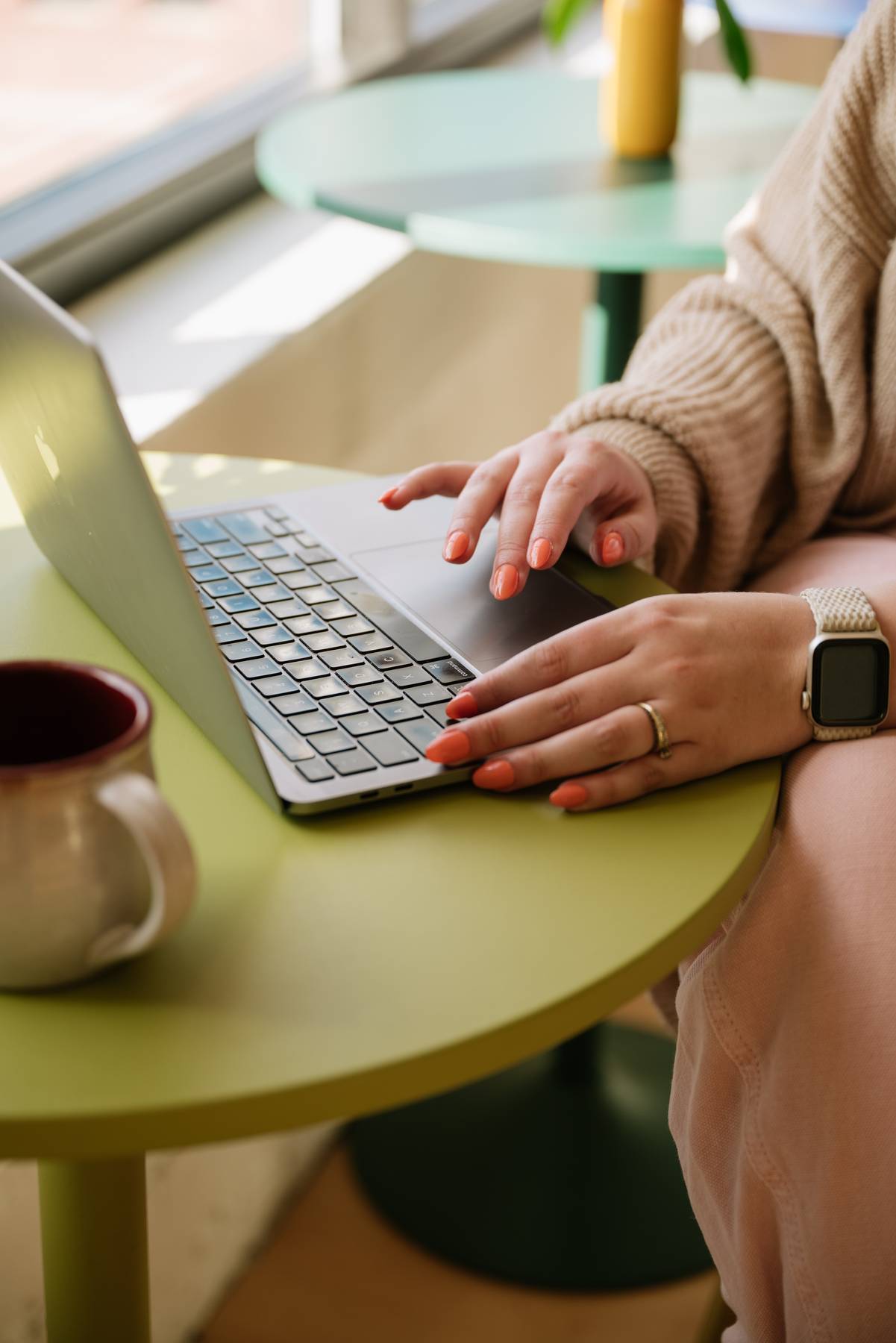 Molli's hands on a laptop at a green café table