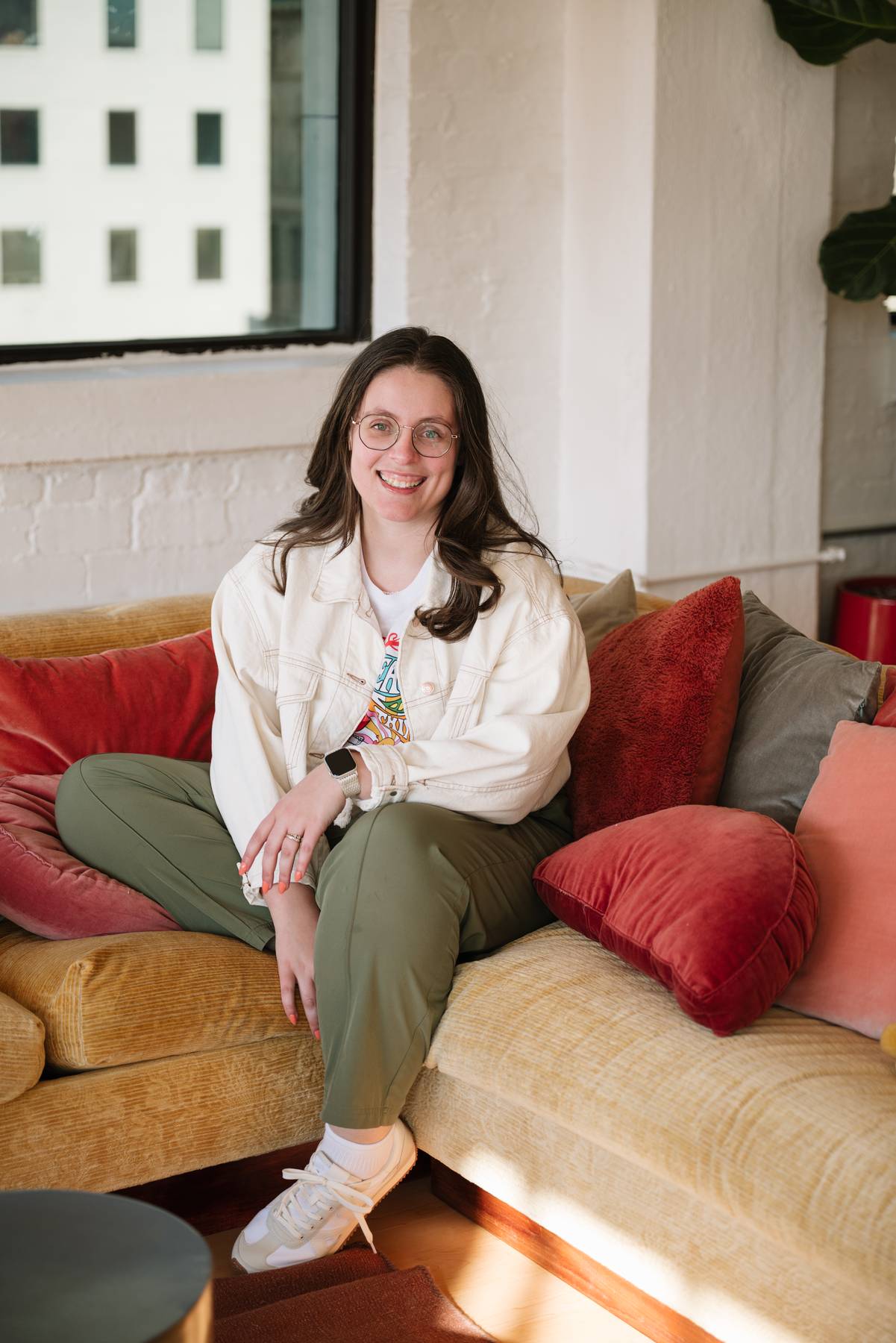 Molli Gorrell smiling on a mustard velvet couch in a cream denim jacket
