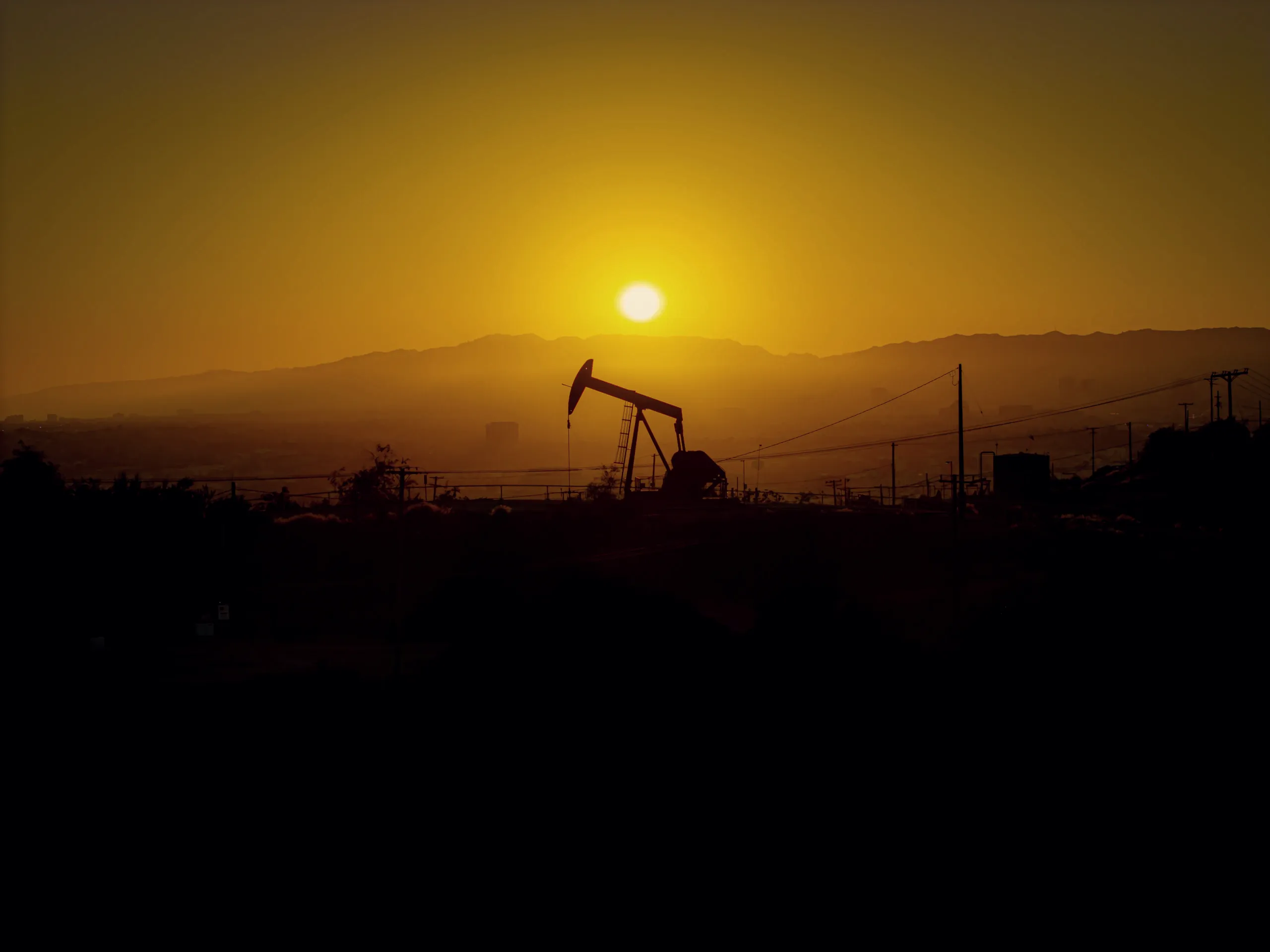 Oil pump jack silhouetted against a hazy Alberta sunset