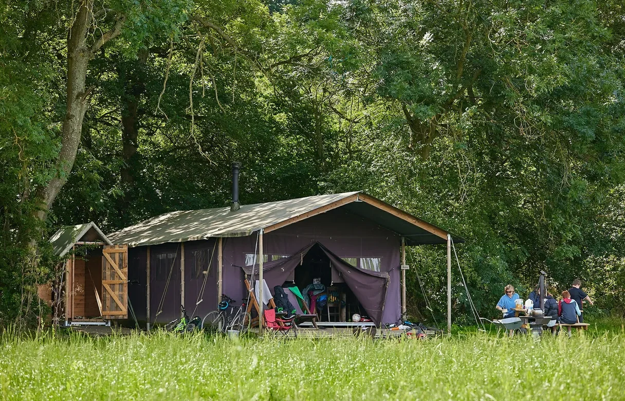 Safari tent nestled in trees with a family sitting at a picnic bench to the side