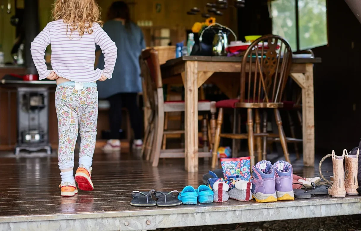 Young girl walking into a glamping tent with shoes and wellies lined up on the right