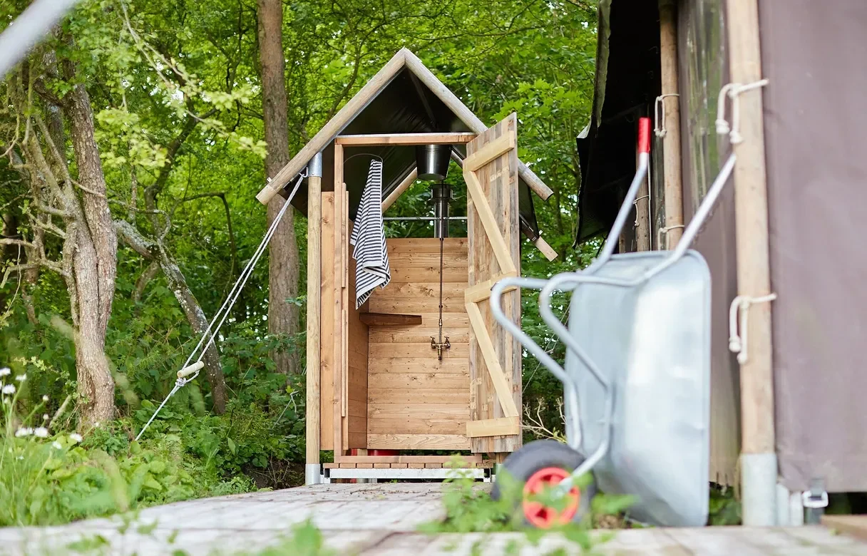 Outdoor shower in a private hut with a wheelbarrow and glamping tent to the right