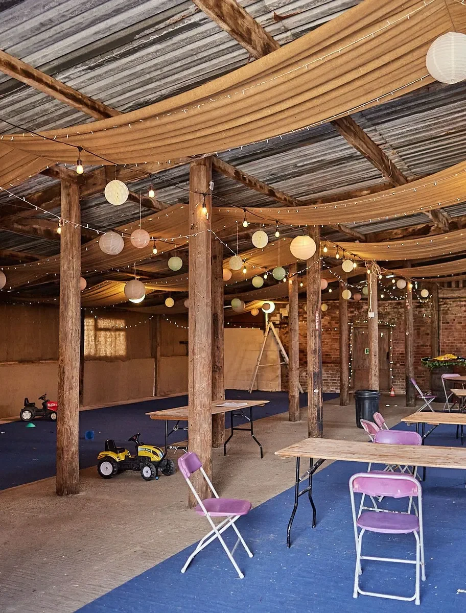 Indoor barn with tables and chairs, ceiling drapes and lights, and a blue carpeted area