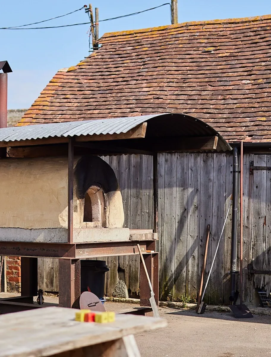 Brick pizza oven under a metal shelter next to a farm building