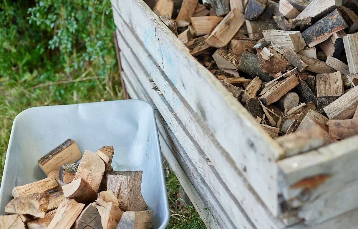 Wheelbarrow of wood chunks next to a large crate filled with firewood