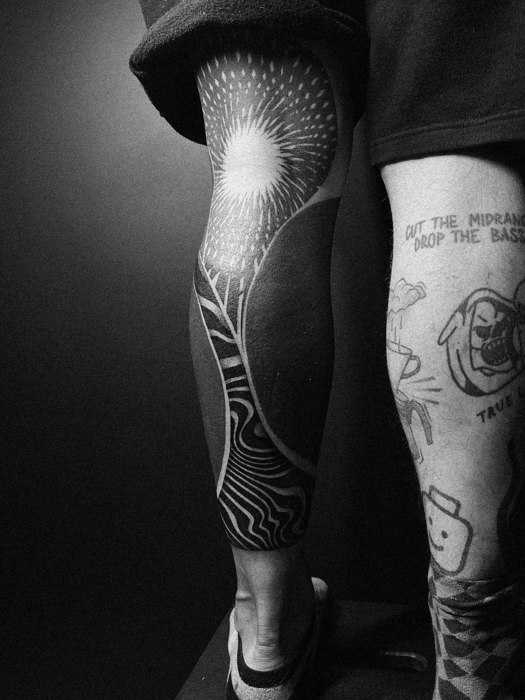 Men's blackwork leg tattoo — flowing linear forms on the back of the calf, with a sun-like form behind the knee. Design by Paweł Kurylak | Photo taken at a tattoo studio in Gdańsk.