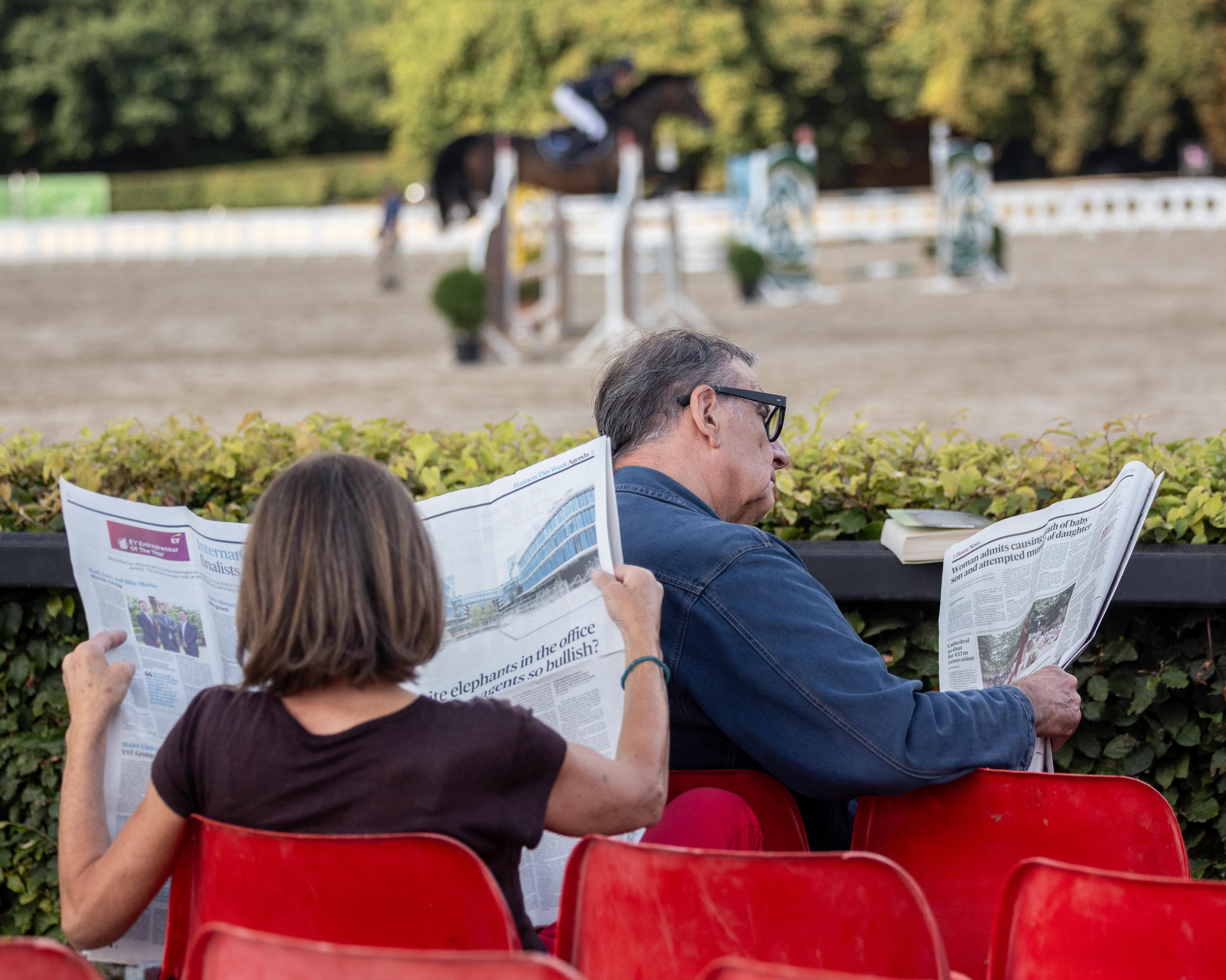 Spectators reading newspapers at an equestrian event