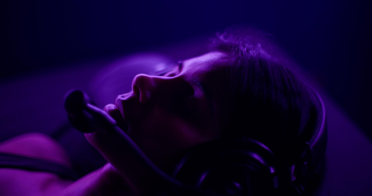 A guest's face in profile, eyes closed, lit violet during a session.