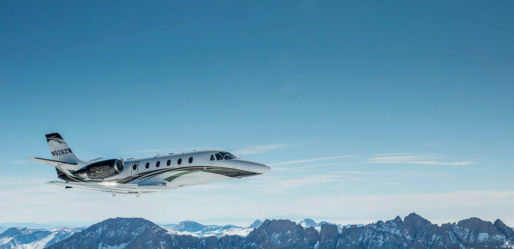 Cessna Citation business jet in flight above snow-capped mountains